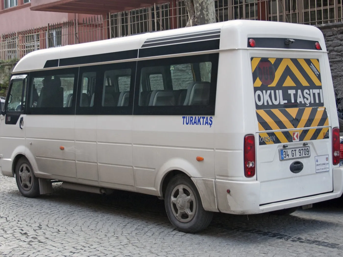 Arkasında okul taşıtı levhası olan beyaz servis minibüsü